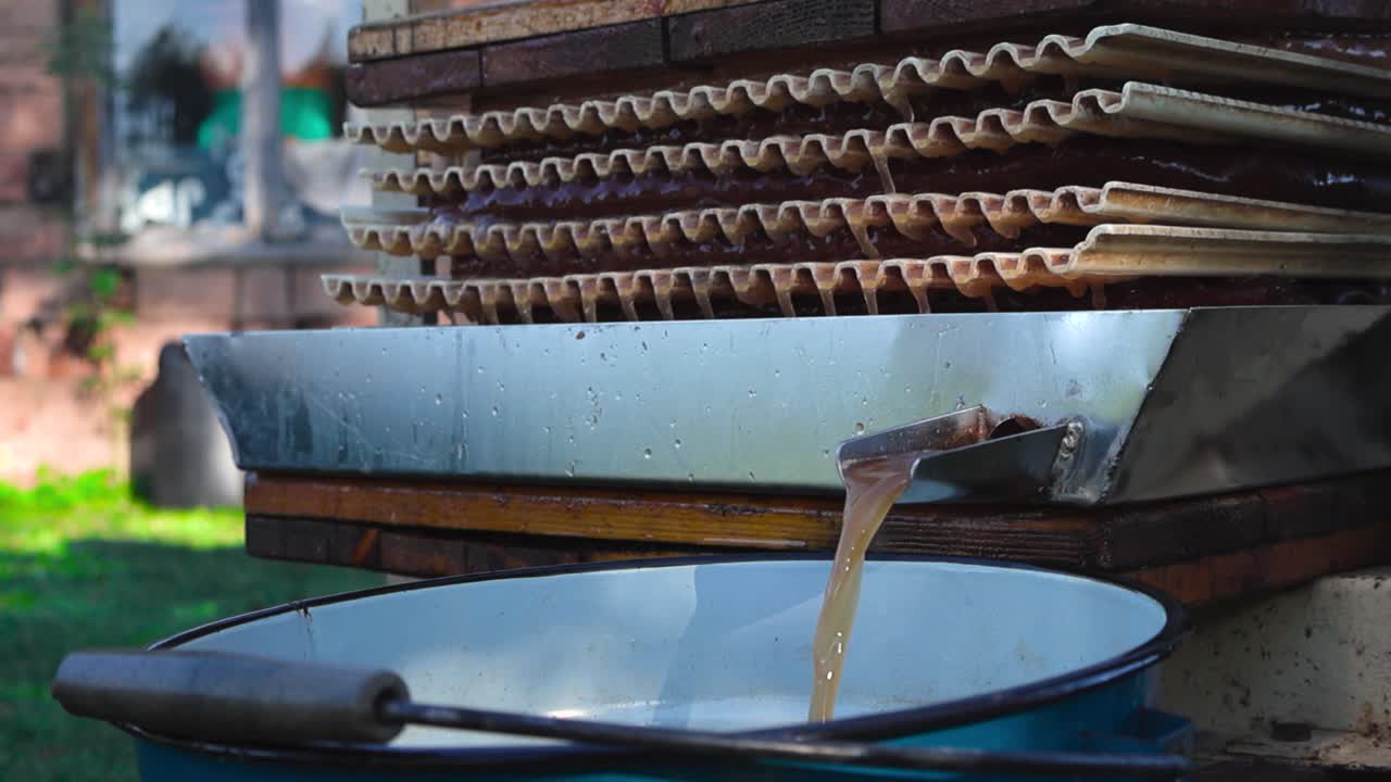 Gorgeous golden brown and yellow apple juice being pressed from apple mush in a sunny garden with a juice press. Bokeh blurry background and shallow depth of field. Juice dripping between press slowly