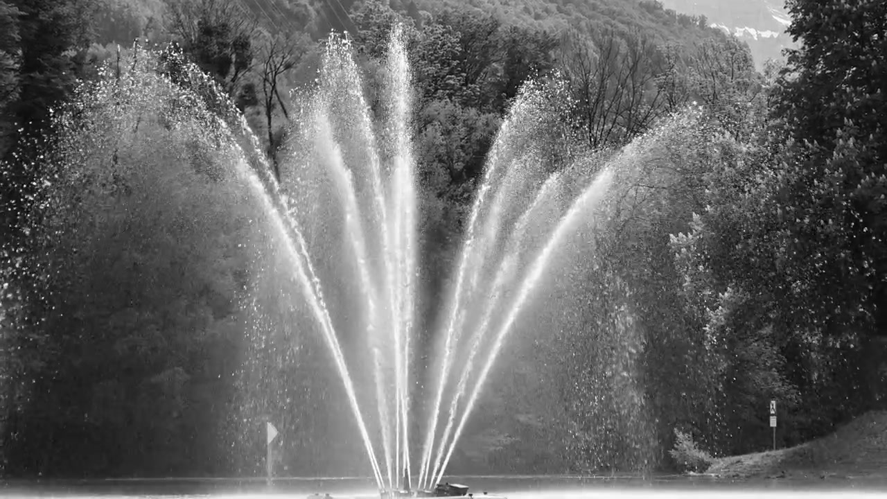 Primo piano di una fontana a più getti sul Walensee, con getti d'acqua che si aprono a ventaglio verso l'esterno, creando una nebbia sottile e goccioline dalla texture visibile.