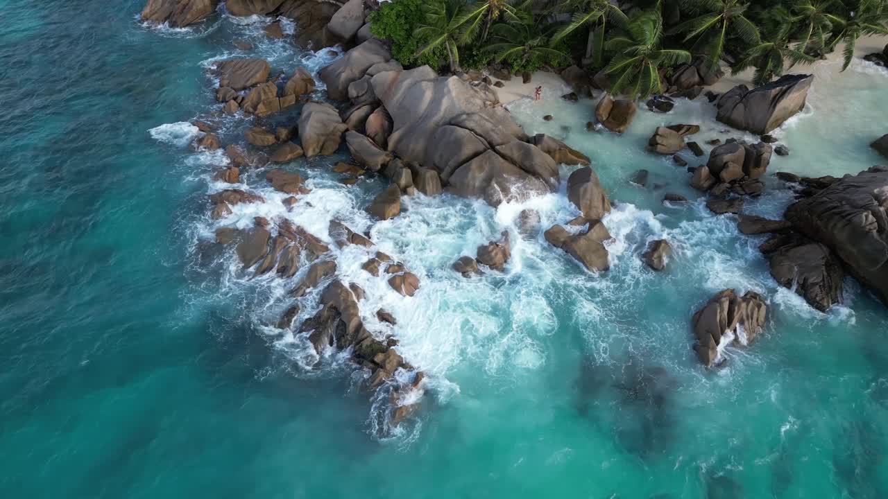 drone rotate around paradise secluded white sand beach tropical island in La Digue Island, Seychelles archipelago Indian Ocean with waves crashes in to rocks aerial top down