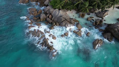 drone rotate around paradise secluded white sand beach tropical island in la digue island, seychelles archipelago indian ocean with waves crashes in to rocks aerial top down
