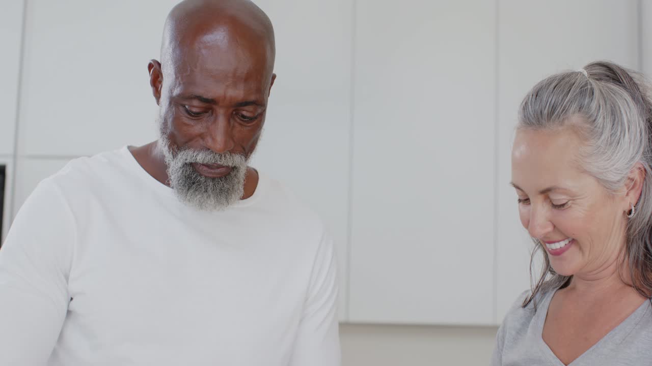 Coppia di anziani afroamericani, uomo e donna, l'uomo che versa la farina mentre la donna prepara la pastella sul bancone