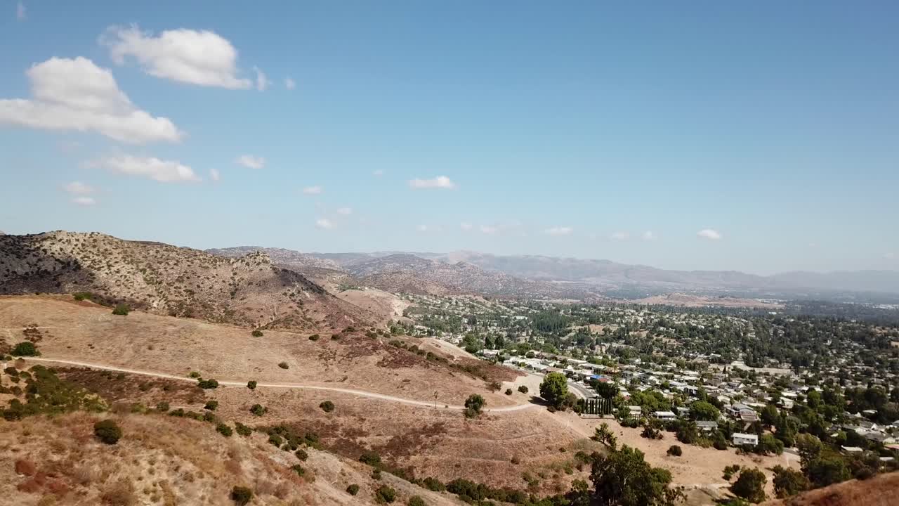 Ripresa con drone in ascesa del paesaggio montano della California e di una piccola città americana nella valle. Case residenziali e appartamenti di lusso in un sobborgo esclusivo. Ampia ripresa panoramica. Hidden Hills, Los Angeles.