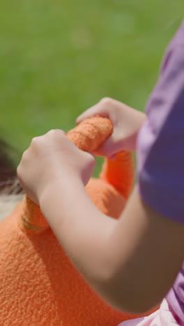 una niña linda con una camiseta púrpura monta un pony con la ayuda del instructor a lo largo del parque de verano verde en un día soleado cerca de la vista trasera en cámara lenta