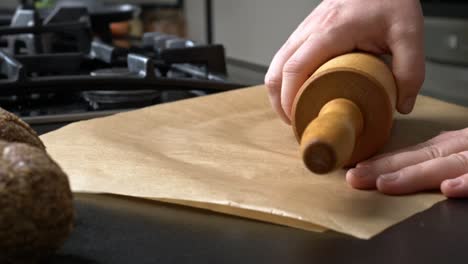 chef rolls dough beneath brown parchment paper with rolling pin
