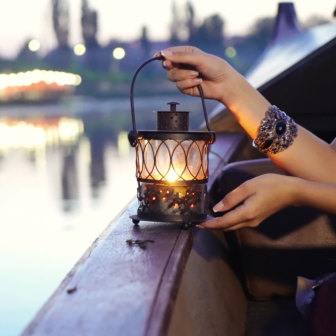 hands of a girl are holding a decorative lantern on a boat in a river near the bank