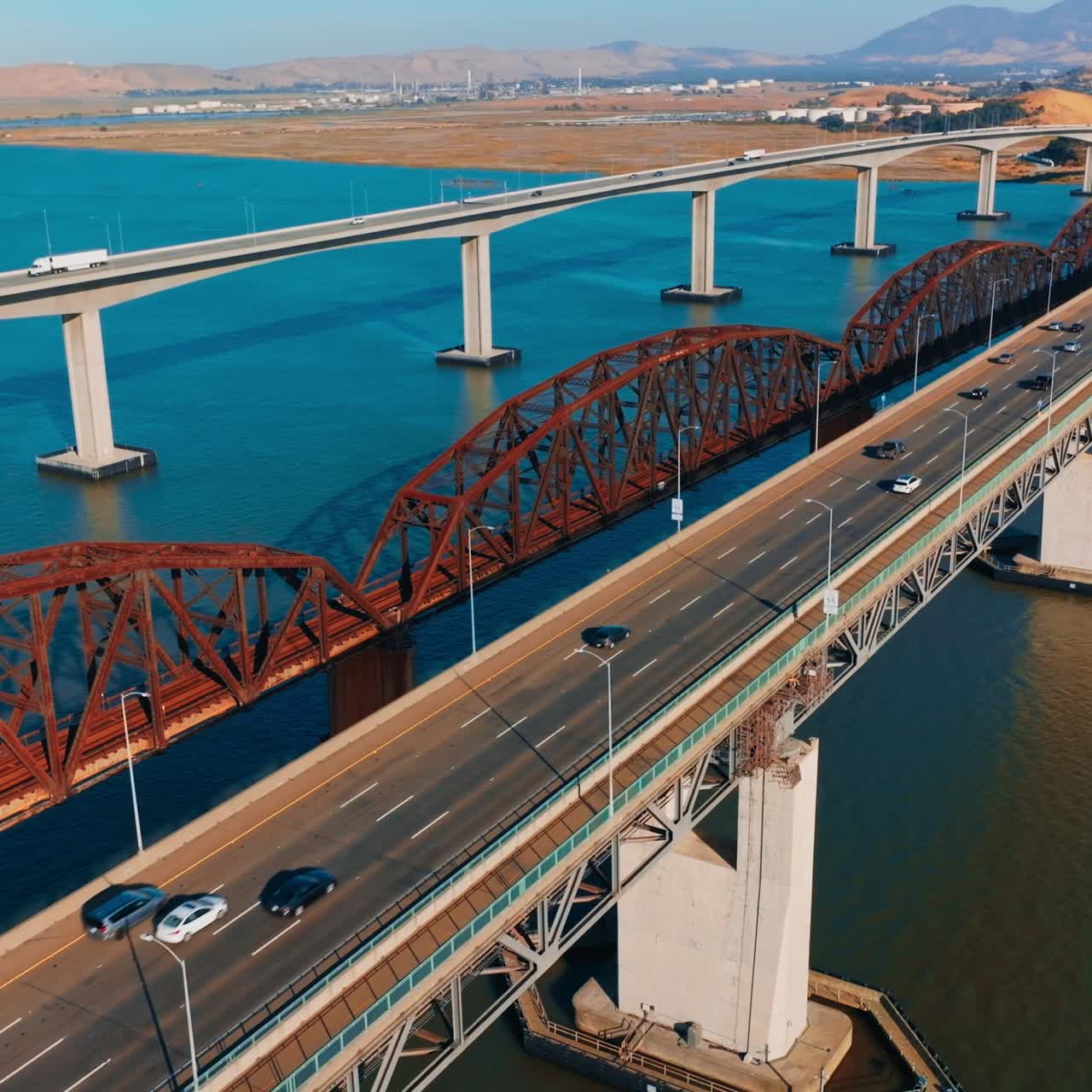 Sunny day footage over the bridges connecting Martinez to Benicia, California, USA. Multiple cars moving by the bridges. Mountainous landscape at backdrop