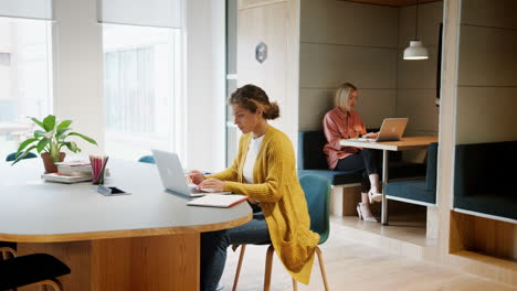 general view of two young adult women working at computers sitting in an office, panning shot