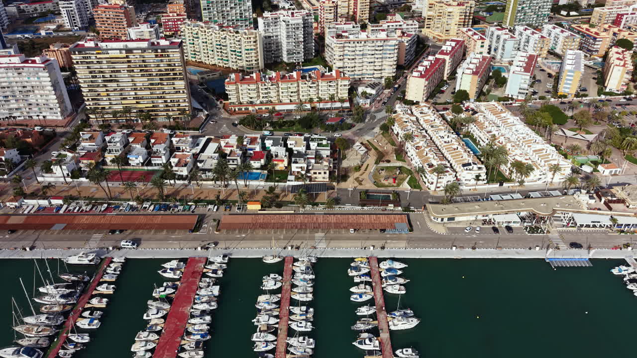 Vista di un porto turistico con barche ed edifici in una zona costiera, in una giornata di sole con cielo sereno, in un vivace contesto urbano.
