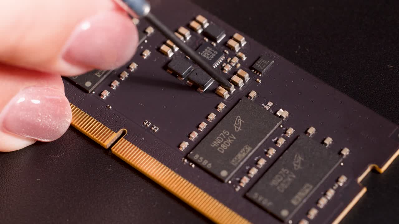 Hand uses fine tool to indicate microchip on circuit board under bright, controlled lighting