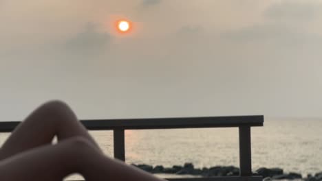 sexy legs of a tanned girl laying on a sun bed at sunrise