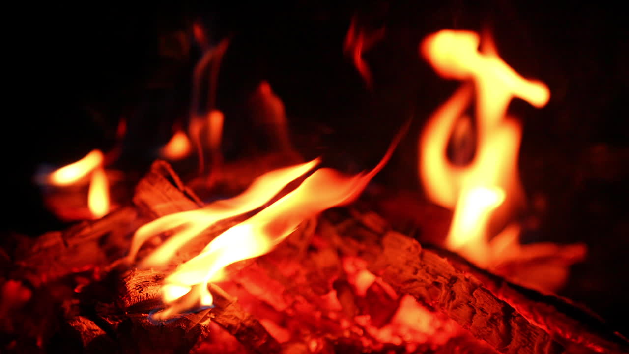 A pile of embers in the almost burnt out bonfire. Little flames are still burning on the wood. Close up. Black backdrop.