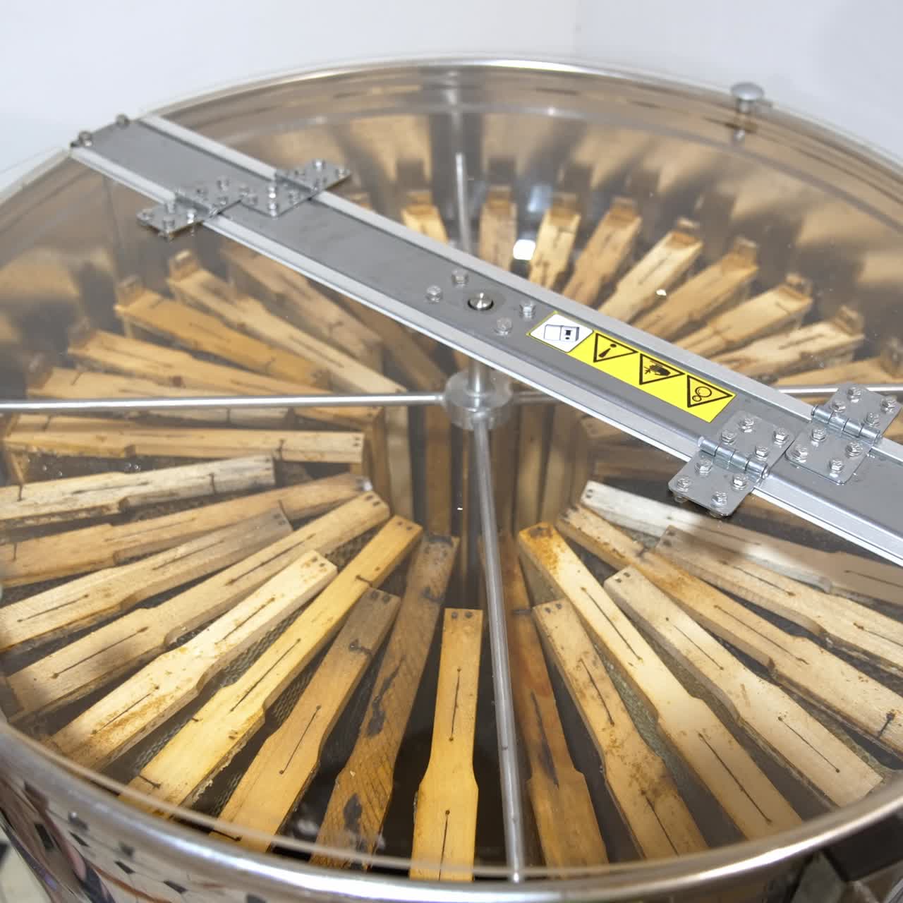 Metal centrifuge device for pumping out honey. Male hand closes apparatus with a transparent lid to avoid splatters