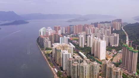 Mehrere-Bootspfade-Auf-See-Mit-Blick-Auf-Die-Skyline-Voller-Bunter-Wolkenkratzer-Von-Ma-On-Shan-Hongkong-Und-Bergsilhouetten-In-Der-Natur