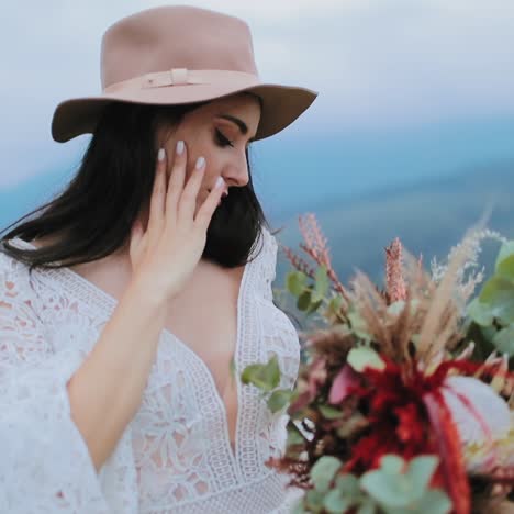 lovely woman in hat and white dress in nature. beautiful model with dark hair holding bouquet of flowers and posing to camera.
