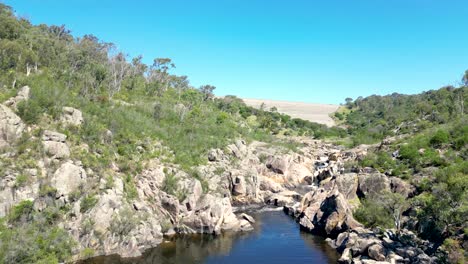 Drone-footage-flying-up-the-Queanbeyan-River-and-then-the-spillway-to-reveal-a-full-Googong-Dam-near-Queanbeyan-in-New-South-Wales,-Australia