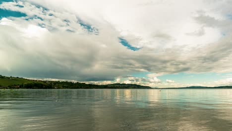 calm waters of lake murten, fribourg, switzerland, reflecting the sky with dramatic clouds sweeping across in this panning timelapse.