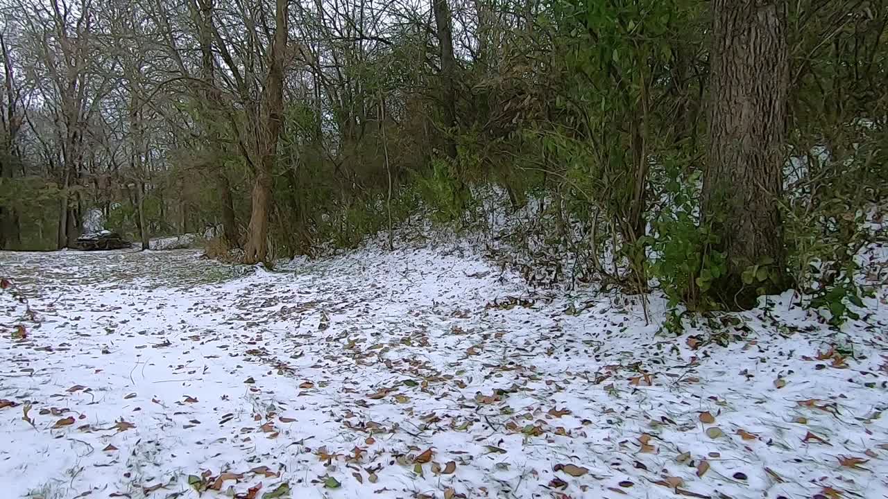POV from the front of off road vehicle while driving across a grassy field covered with a light snow on a cloudy winter afternoon, ending in a wooded area