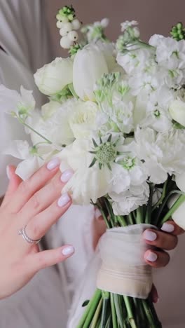 Charming-bride-in-a-white-top-holding-a-wedding-bouquet-of-white-roses,-tulips-and-other-flowers