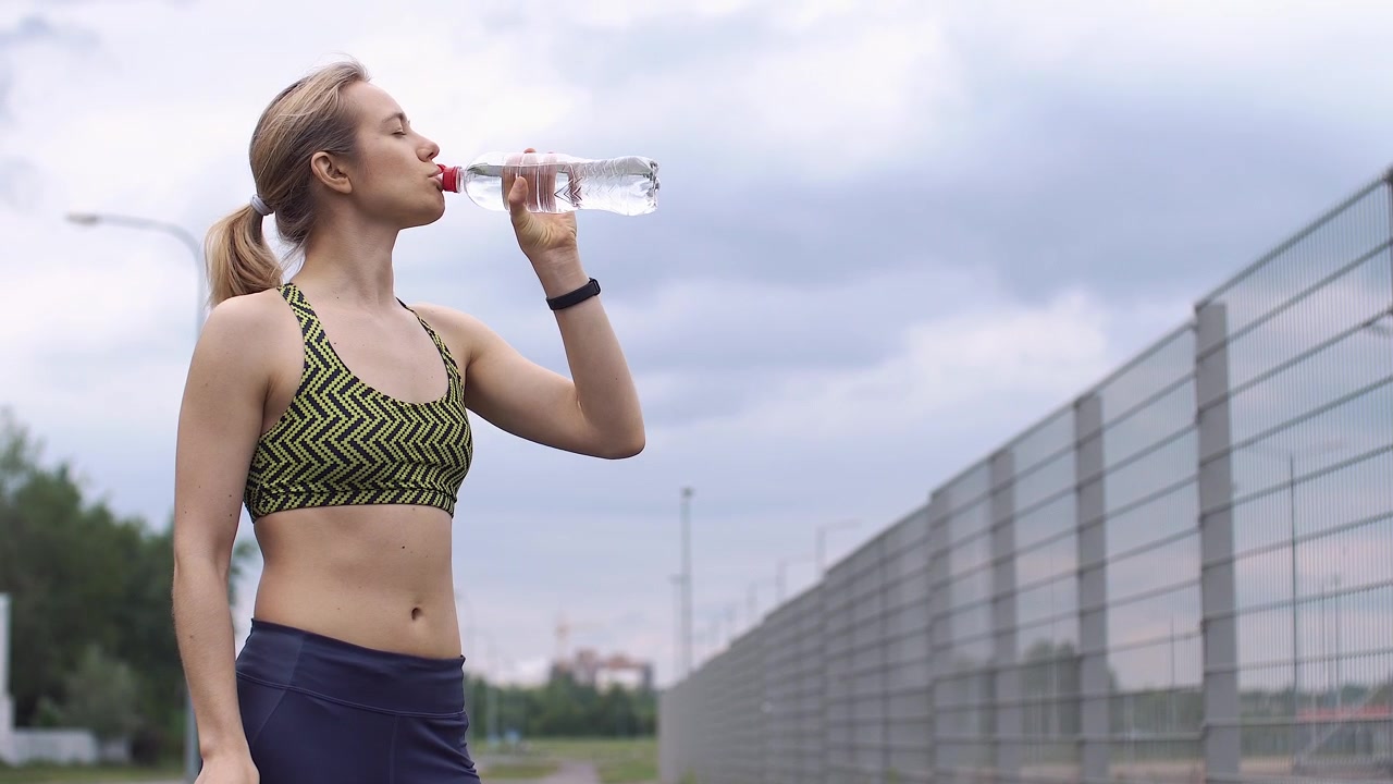 Atleta donna che si prende una pausa per bere acqua durante l'allenamento all'aperto
