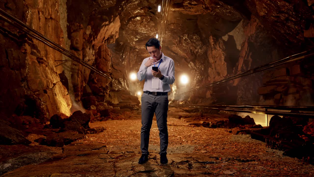Full Body Of Asian Male Professional Worker With His Smartphone In Underground Mine Tunnel, He Is Nodding His Head With Dissapionted