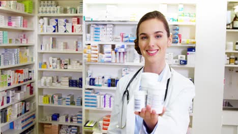 farmacéutico sonriente mostrando el recipiente de la medicina en la farmacia