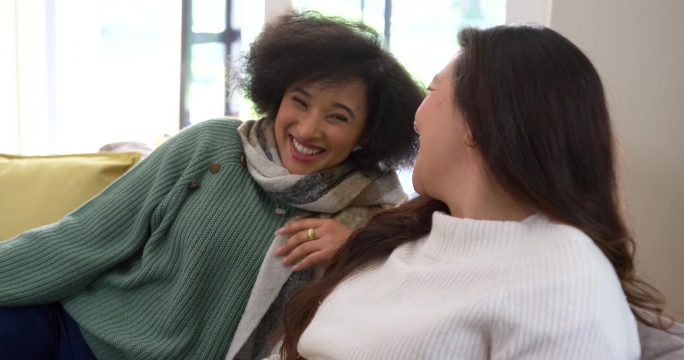 Amiche di diverse etnie sul divano che sorridono, toccano una sciarpa e reagiscono a un segnale fuori campo.