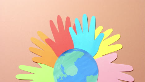close up of hands together with globe made of colourful paper on brown background with copy space