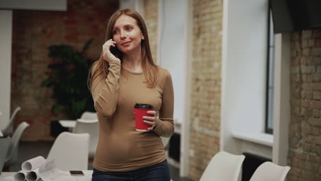 trabajadora joven haciendo una llamada en la oficina. espacio de copia. mujer de negocios hablando por teléfono y tomando un café.