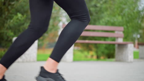 sporty woman jogging in black leggings and sneakers, background with concrete bench and trees, showcasing an active lifestyle, fitness, and workout routine in park
