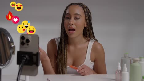 gen z woman filming ugc make up tutorial or review for social media on mobile phone with motion graphics emojis showing multiple notifications liking and reacting to online content