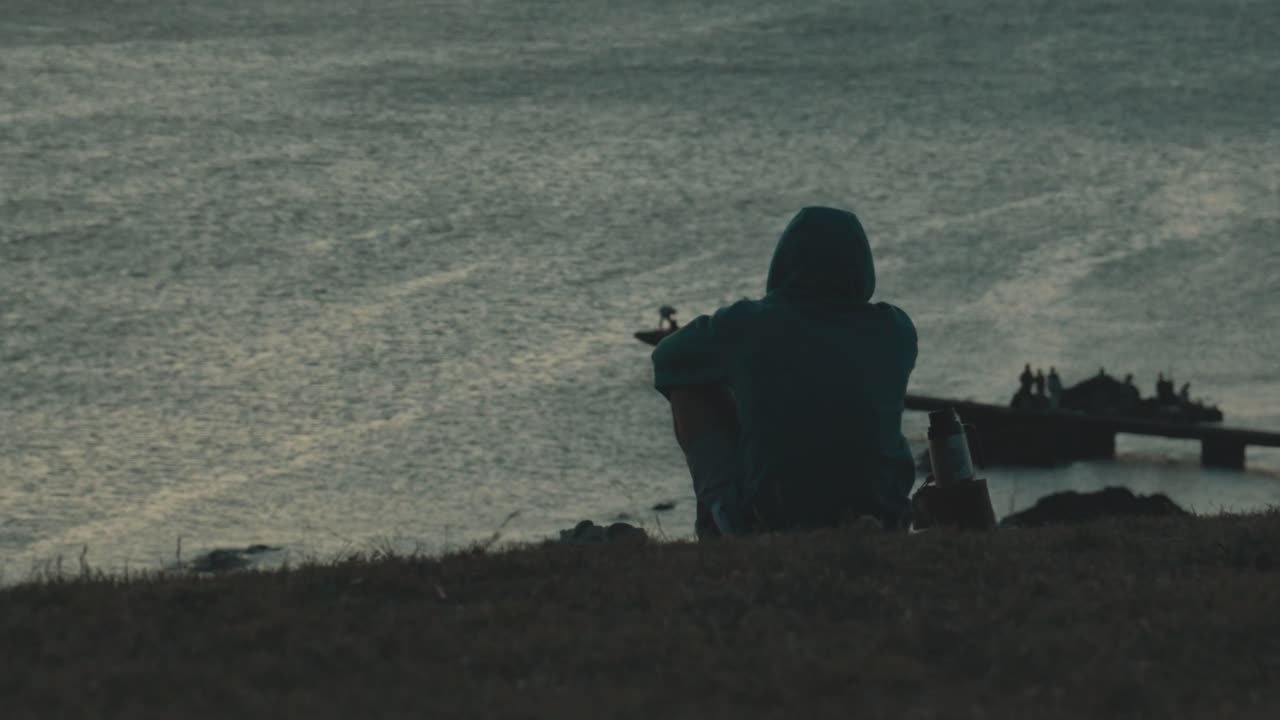 Sagoma malinconica di un uomo pensieroso e solitario seduto su una scogliera che guarda l'oceano. Solitudine e contemplazione in un paesaggio drammatico