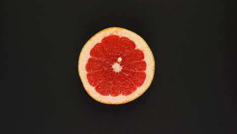 rotating grapefruit on a black background. fresh juices, fruits, vitamin and summer concept. top view of half a juicy citrus