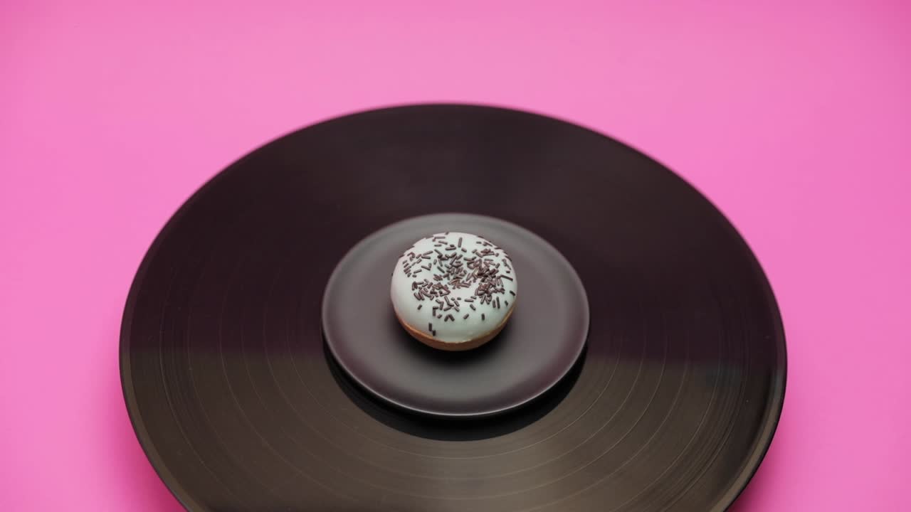An American donut topped with blue chocolate with black choco crumbs turns in a circle on a black turntable. The shot from above