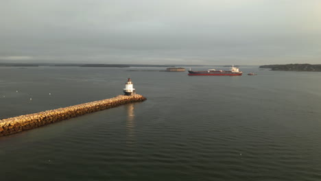 the spring point ledge lighthouse off the coast of maine with large shipping vessel in background