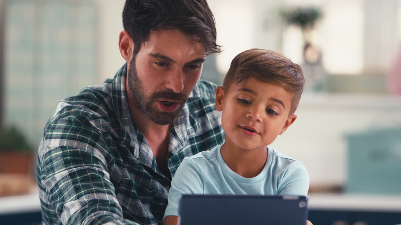 primer plano del padre en casa en la cocina con su hijo transmitiendo o jugando en una tableta digital