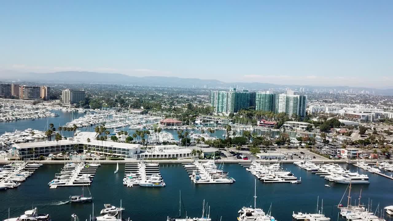 Marina del Rey Hotel at port harbor surrounded by yachts and boats in summer. Luxury condos and apartment buildings in background. Blue sky in Los Angeles, California