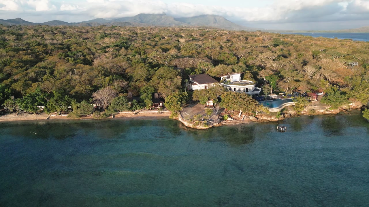 Stunning drone aerial capturing lush forest, clear ocean, and distant mountains around Menjangan Island in West Bali National Park, showcasing untouched tropical beauty and scenic coastal landscape.