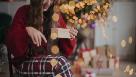 mujer alegre abriendo una caja de regalos de madera en una casa decorada durante navidad