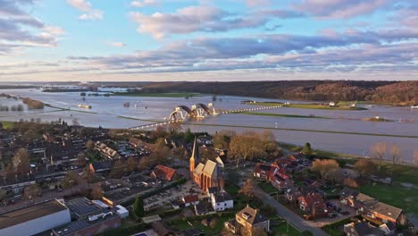 flyover drone shot over the town and church of driel with the weir of driel in the background and door of the weir open during high waterlevels