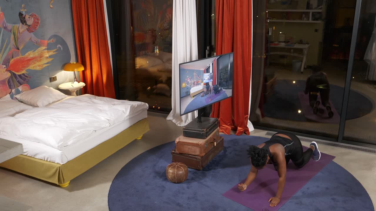 bajando en su alfombra de yoga púrpura, la mujer está fortaleciendo su núcleo haciendo planking mientras apoya su peso usando sus codos y dedos de los pies