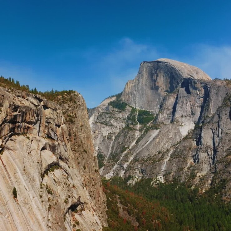 Câmera lenta se aproximando das falésias no Parque Nacional de Yosemite, Califórnia, EUA. Pinheiros crescendo na base da montanha