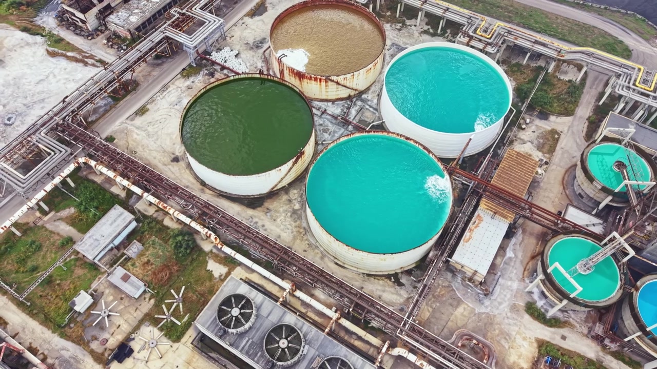 Industrial tanks filled with liquids at a processing facility near a river during daylight hours