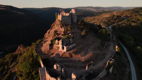 aerial-view-tilting-down-over-the-castle-of-couzan-at-sunrise,-french-fortress-in-Loire-departement,-French-countryside