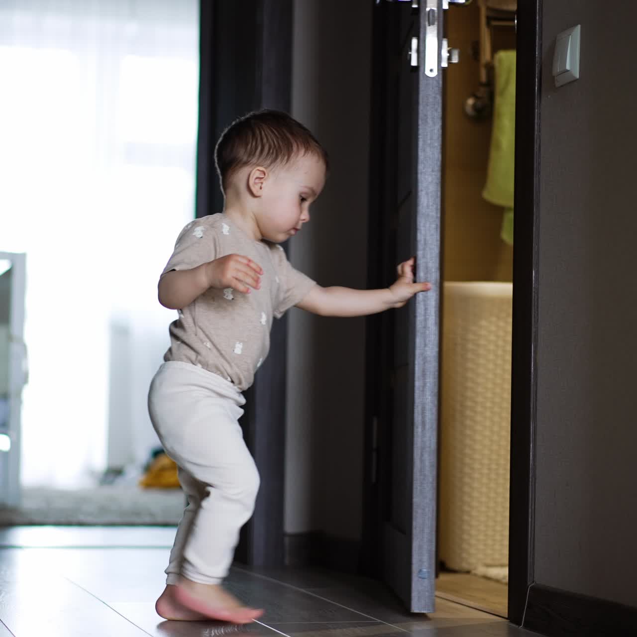 Cute baby boy comes up to an open door. Kid stops for a moment and then closes the door
