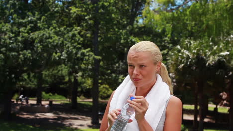 a woman walks and takes a drink before wiping her head and walking again