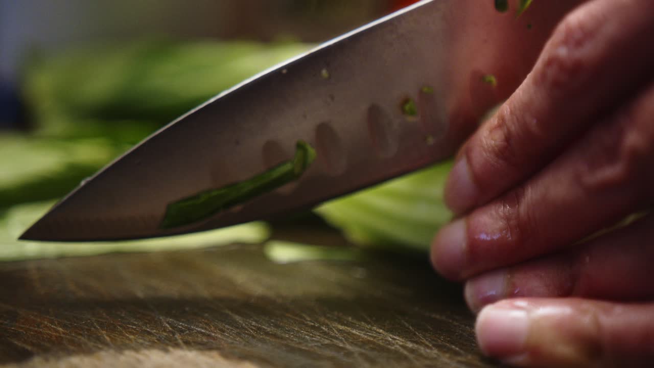 Detail of Asian chef slicing leafy green vegetable with sharp knife.