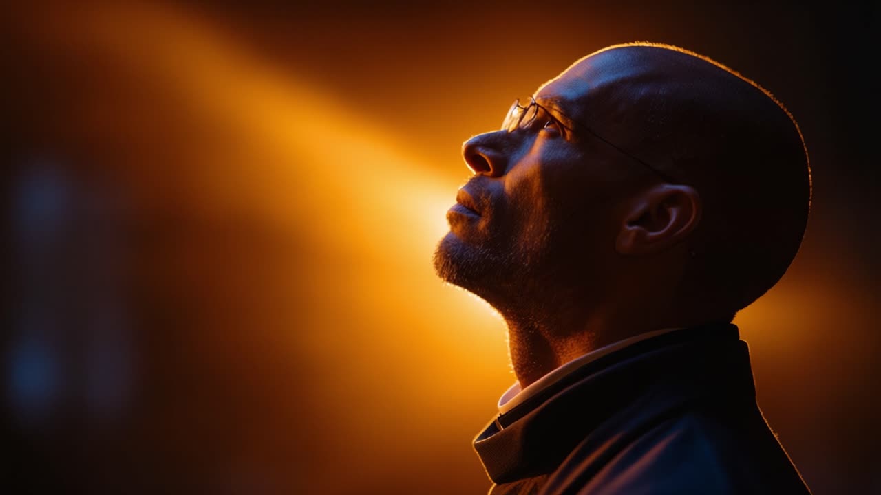 A contemplative man gazes upward, bathed in warm orange light that highlights his features, capturing a moment of reflection and inspiration against a dark backdrop