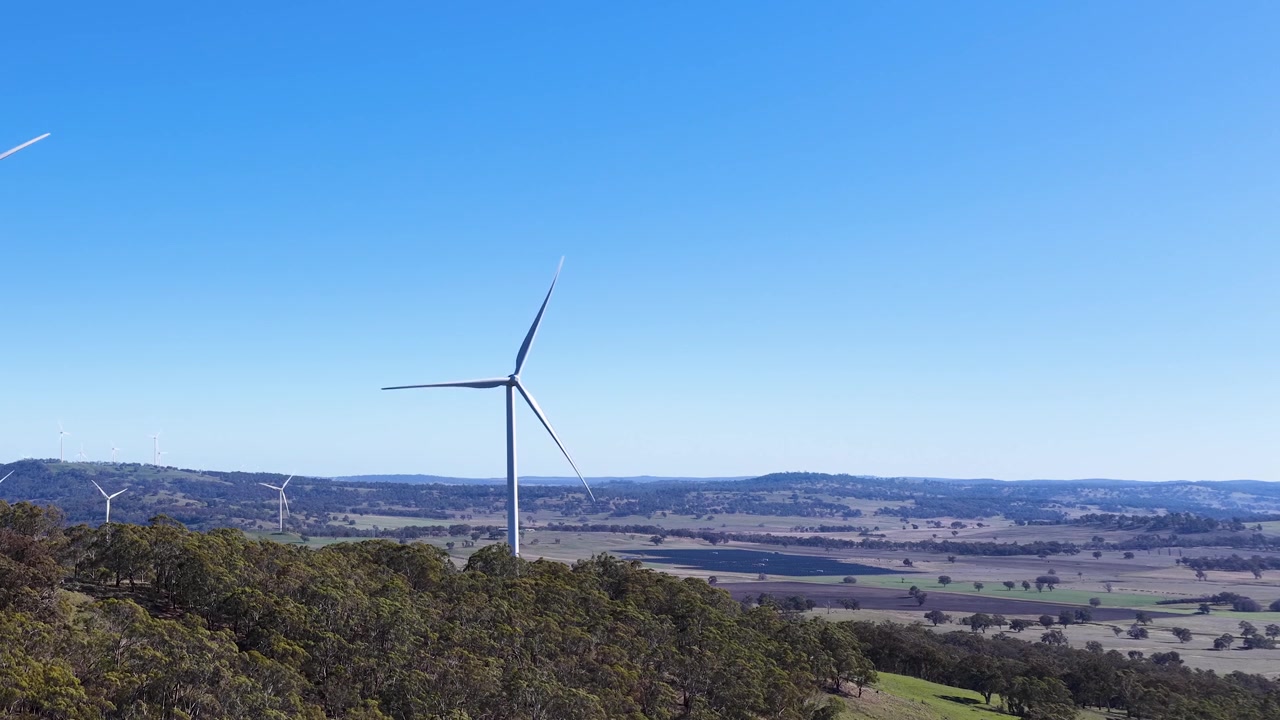 Turbina eolica in rotazione in un paesaggio rurale sotto un cielo azzurro limpido
