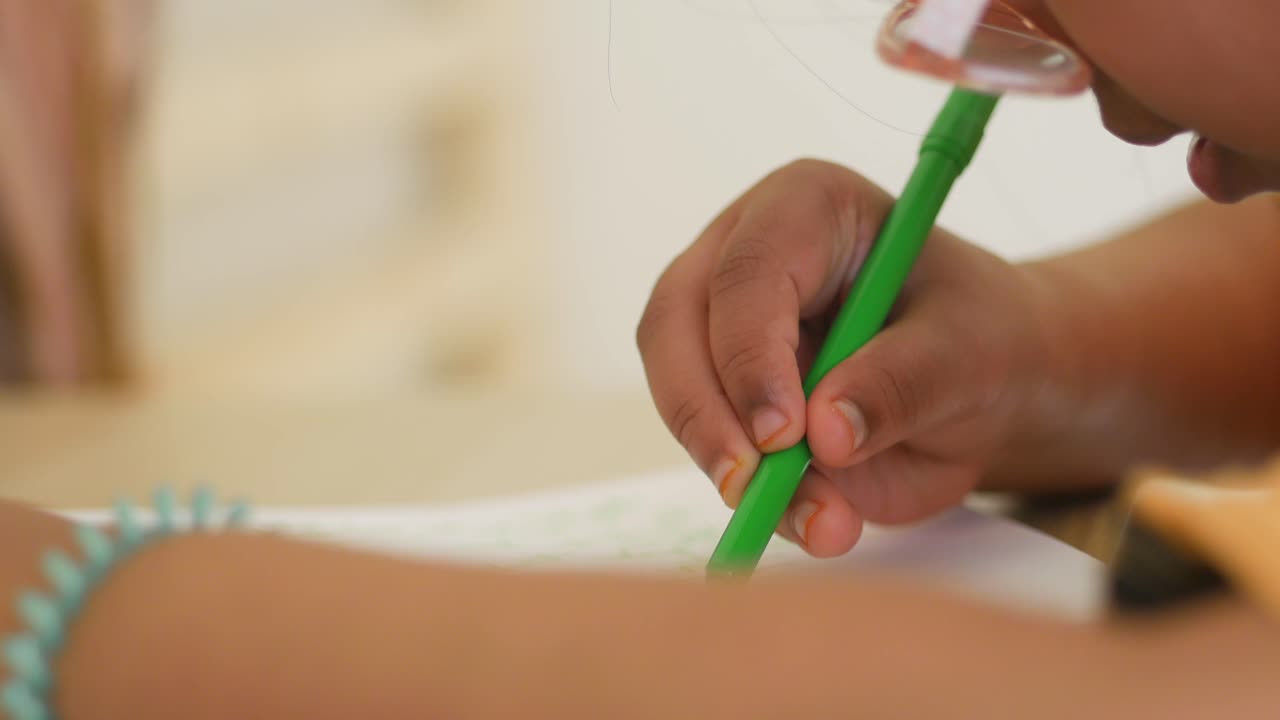 Close-up of a child's hand drawing with a green marker
