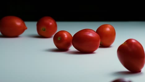 slow motion food: a large quantity of tomatoes tumble onto a black and white mirrored surface, bouncing and rolling back in a playful, mesmerizing motion